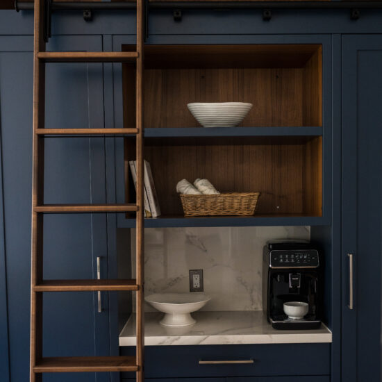 Elegant navy blue kitchen cabinetry with a built-in coffee station, marble backsplash, and a sliding ladder for high storage, designed for a luxury home in Oshawa.