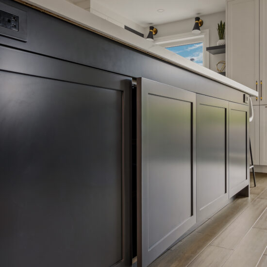 Close-up of a custom dark cabinetry kitchen island in a Whitby home, featuring hidden storage, elegant paneling, and a sleek quartz countertop