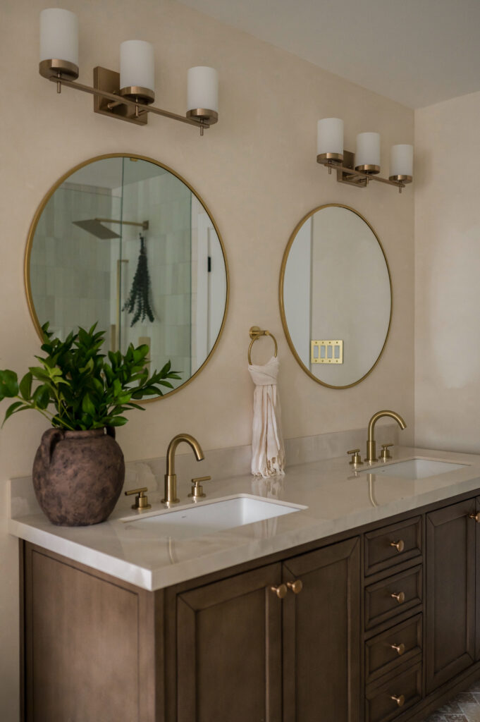 Elegant bathroom renovation in Oshawa, Ontario, featuring a double vanity with gold fixtures, round mirrors, and soft neutral tones for a timeless and sophisticated design.