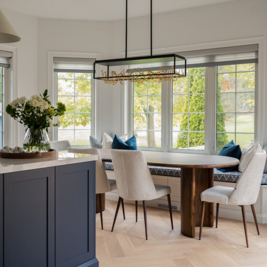 Bright, contemporary dining space featuring a wooden table, upholstered chairs, built-in window seating, and modern lighting, designed by MM Interior Design serving Whitby, Oshawa, and Clarington.