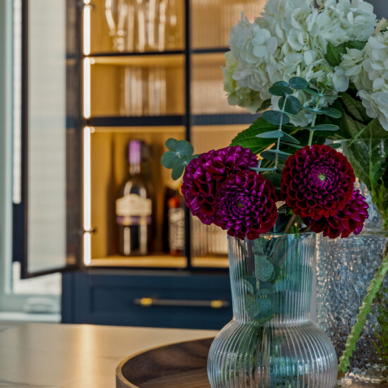 Close-up of a beautifully styled kitchen in Whitby, featuring fresh floral arrangements, a marble countertop, and a backlit glass cabinet showcasing elegant decor.