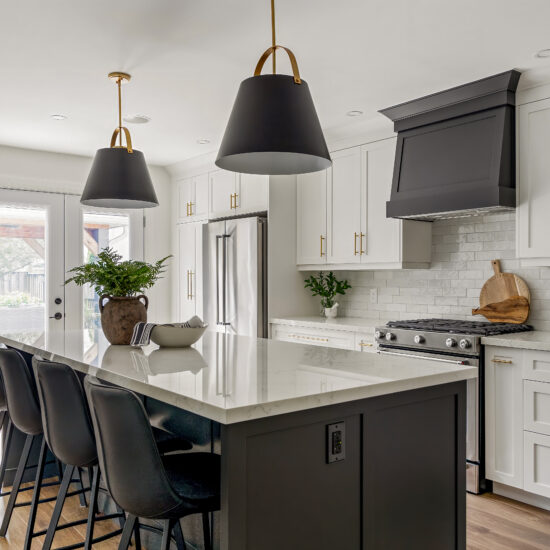 Luxury modern kitchen featuring a large black island with white marble countertop, black leather barstools, pendant lighting with gold accents, white shaker cabinets, and a black range hood.