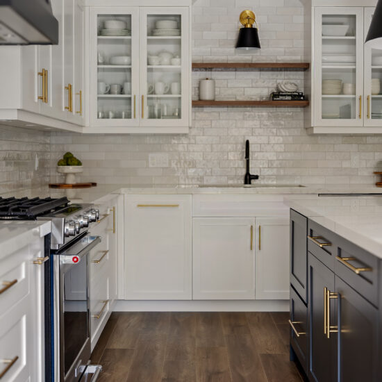 Luxury white kitchen with black island, gold hardware, open wood shelving, and high-end stainless steel appliances in Durham Region.