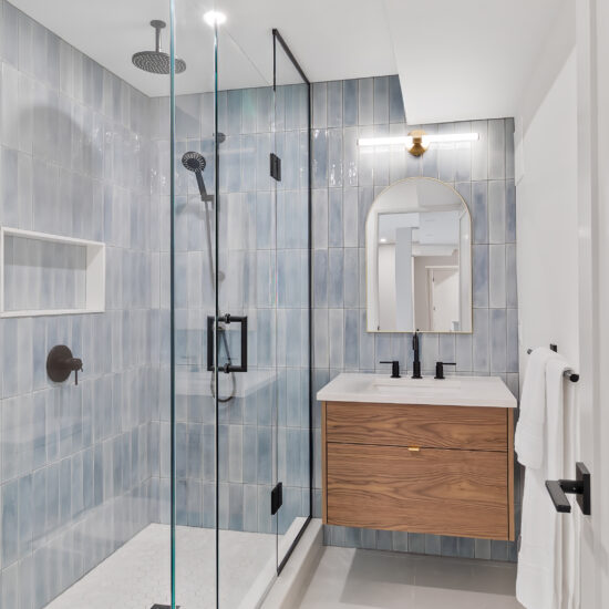 Modern bathroom featuring a spacious glass-enclosed shower with blue tile walls, a floating wood vanity, and matte black fixtures in a Whitby home.