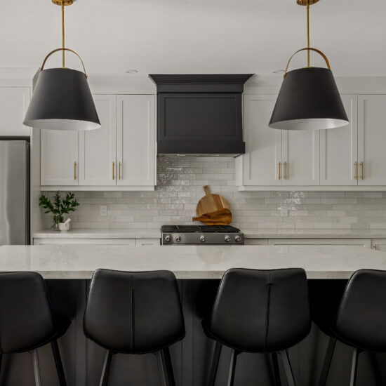 Modern black and white kitchen with a large quartz island, black leather barstools, matte black range hood, and oversized pendant lighting in Durham Region.