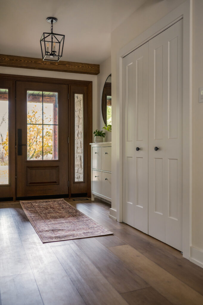 Warm and inviting modern entryway design in Whitby, Ontario, featuring a wood front door, natural light, and a cozy area rug for a welcoming home entrance.