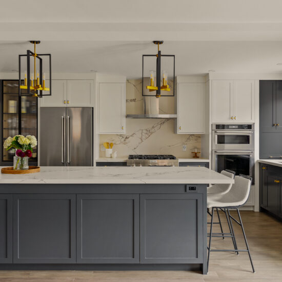 Modern kitchen featuring a large island with dark cabinetry, white upper cabinets, gold-accented lighting, marble countertops, and high-end appliances, designed by MM Interior Design for homes in Whitby, Oshawa, and Clarington.