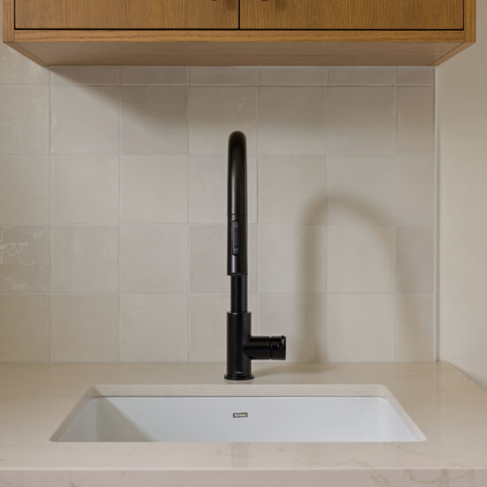 Modern laundry room sink with a matte black faucet, oak cabinetry, and neutral tiled backsplash in a Whitby home.
