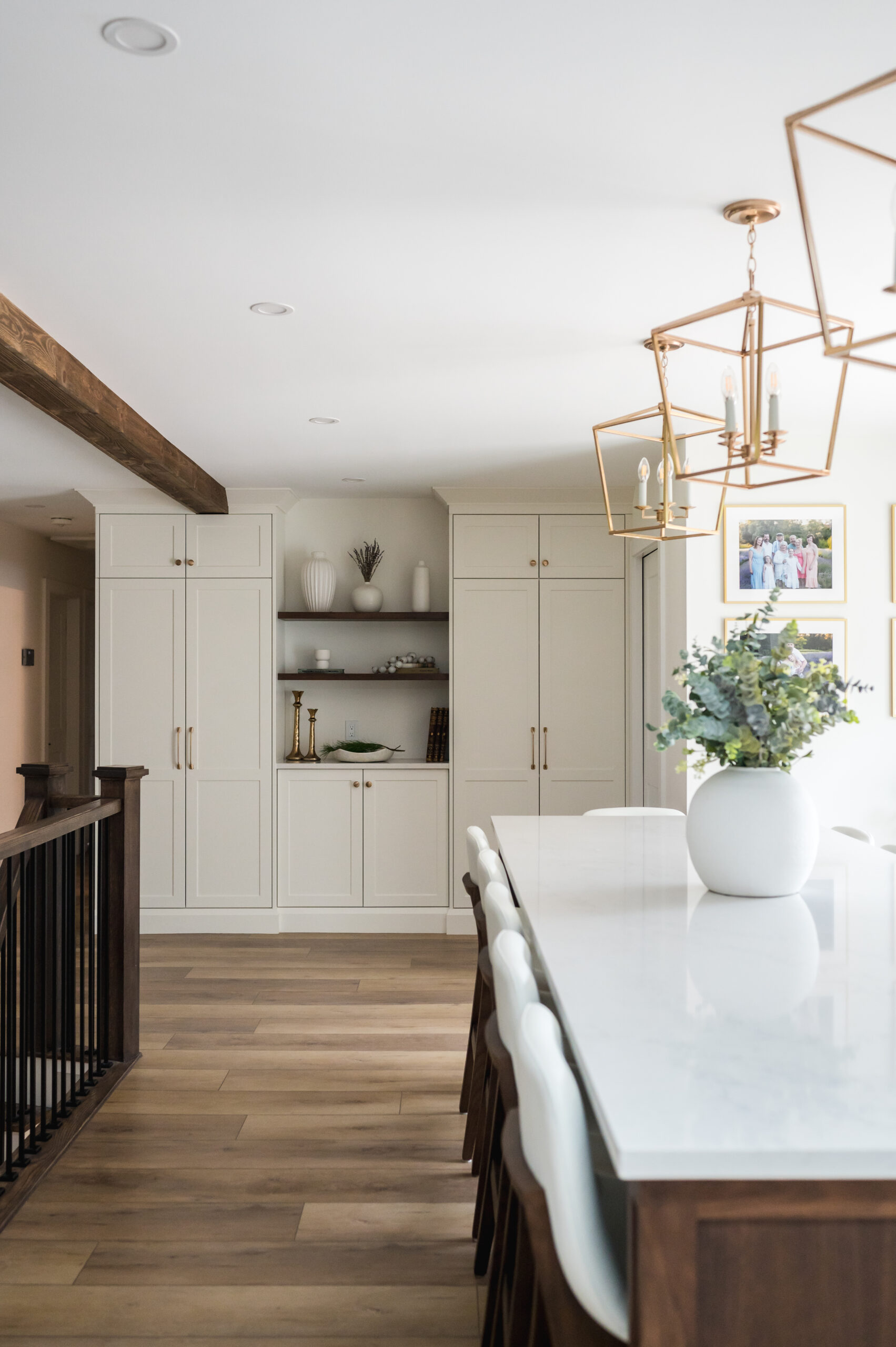 Modern Clarington kitchen featuring custom white pantry cabinetry, gold hardware, and dark wood open shelving next to a large white island.