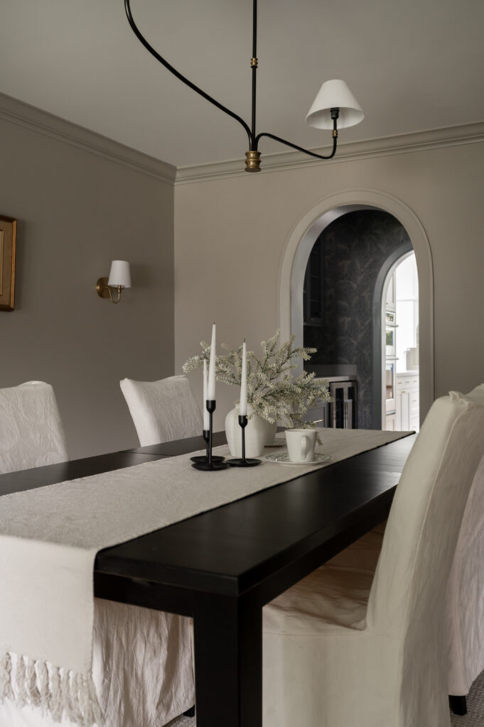 Sophisticated dining space design in Uxbridge featuring a black dining table, white slipcovered chairs, a modern black chandelier, and a classic arched entryway. Perfect inspiration for a transitional or organic modern home remodel.