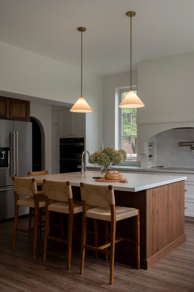 A large walnut wood kitchen island in an Uxbridge home with a white countertop, three woven bar stools, and two elegant pleated pendant lights hanging above.