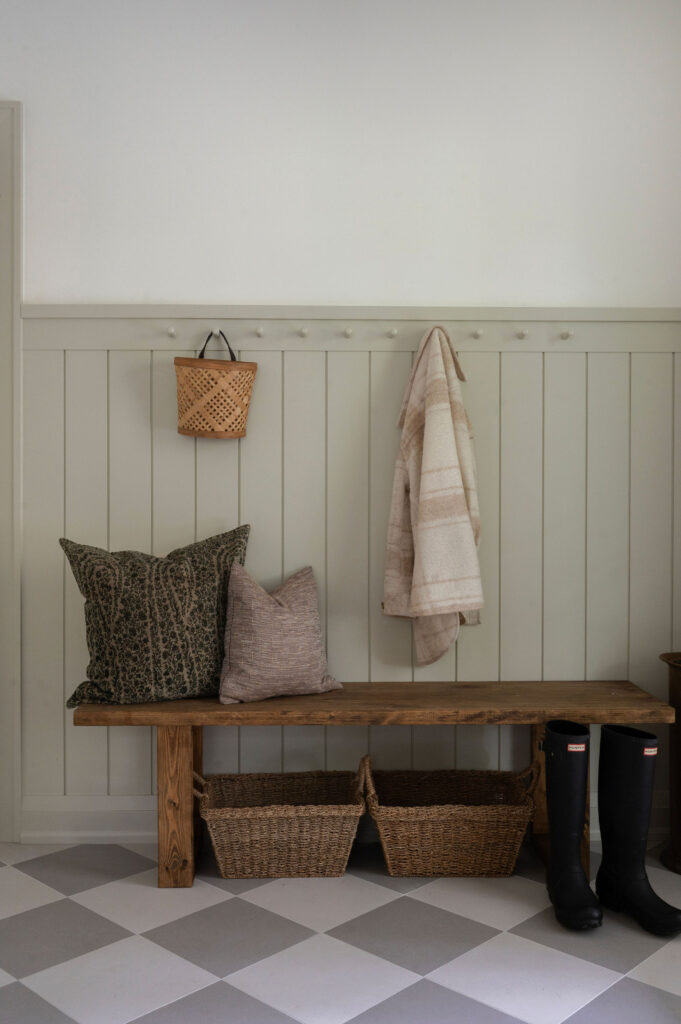 A mudroom in Uxbridge featuring a rustic wood bench, grey and white checkered tile floors, and sage green vertical slat wainscoting with coat pegs.